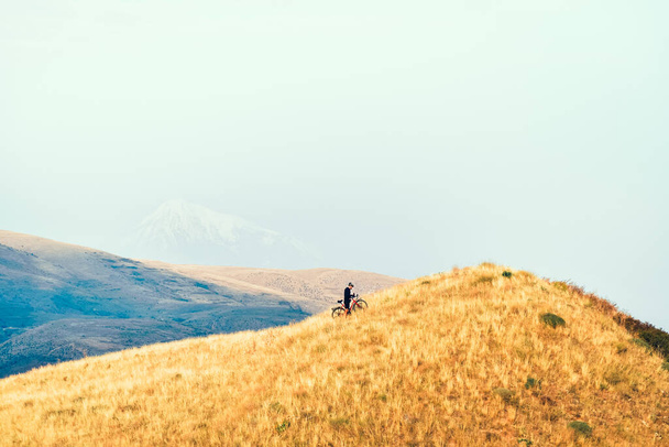 Caucasian male cyclist push bicycle uphill in armenia mountains. Bicycle touring adventure lifestyle concept. Application use and navigation concept. Got lost in wilderness cyclist - Photo, Image