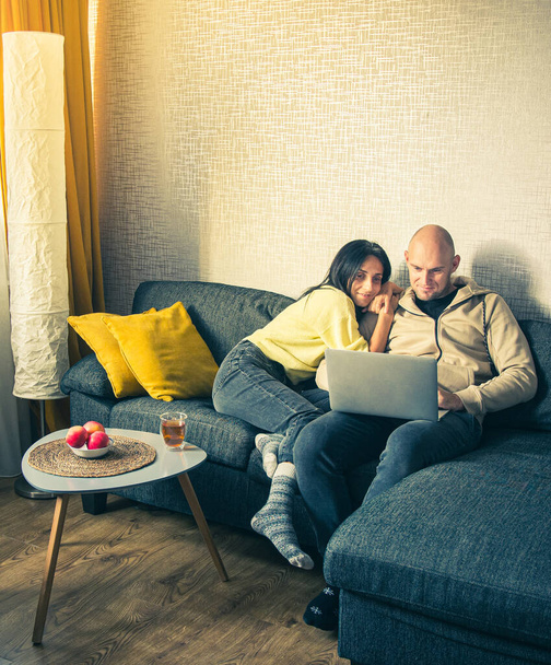 Schönes junges Paar, das gemeinsam mit dem Laptop surft, shoppt gemütlich lächelnd intim, während es zu Hause auf dem Sofa sitzt - Foto, Bild