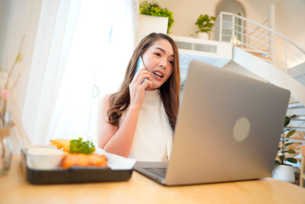 Asian woman with curly hair is working chatting with clients or colleagues via communication channels, telephone, internet with her laptop and mobile phone. - Фото, зображення