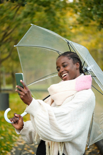 Africká žena brát selfie s chytrým telefonem a průhledný deštník s úsměvem na podzim. - Fotografie, Obrázek