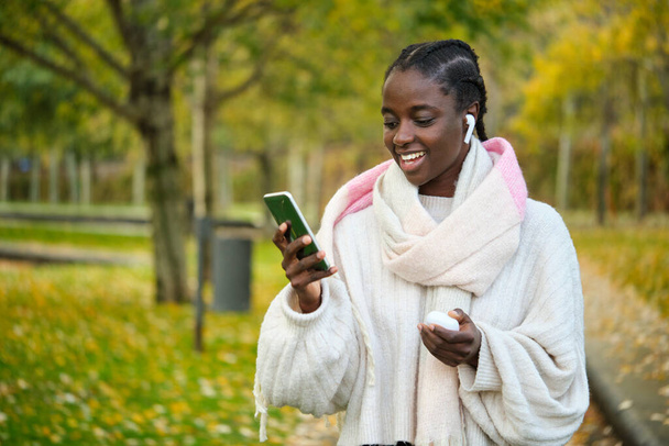Muotokuva afrikkalainen nainen hymyilee ja kuuntelee musiikkia syksyllä. - Valokuva, kuva