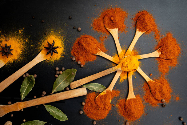 Paprika, curcuma et feuilles de laurier disposées comme des fleurs sur des cuillères à thé en bois sur fond noir - Photo, image