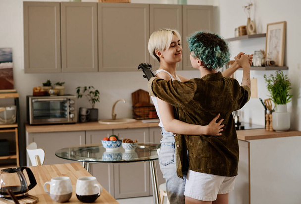Νεαρό ζευγάρι λεσβιών που χορεύουν μαζί στην κουζίνα στο σπίτι - Φωτογραφία, εικόνα