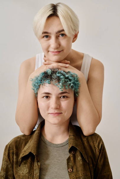 Vertikální portrét mladého páru lesbiček hledících na kameru na bílém pozadí - Fotografie, Obrázek