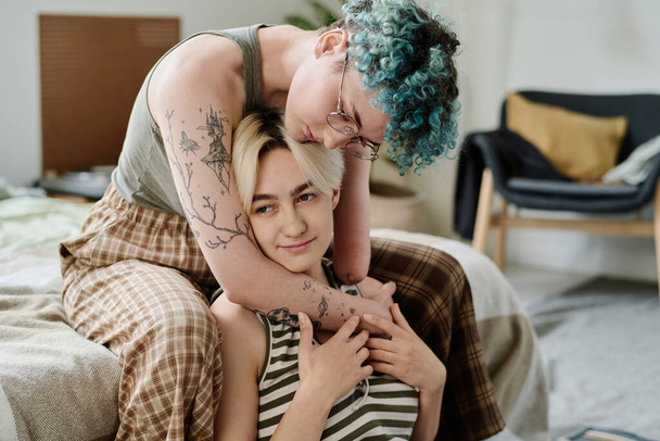 Junge Frau mit amputiertem Arm umarmt ihre Freundin, während sie zu Hause sitzt - Foto, Bild