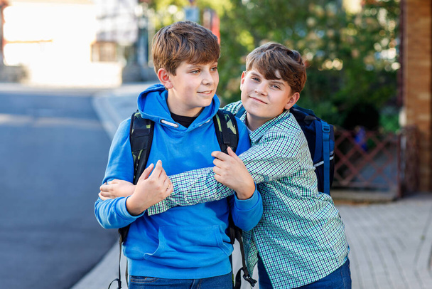 Два мальчика с рюкзаком или сумкой. Школьники по дороге в школу. Здоровые улыбающиеся дети, братья и лучшие друзья на улице покидают дом. Возвращайся в школу. Счастливые братья и сестры - Фото, изображение