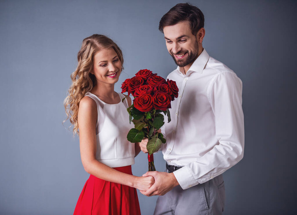 Beau couple élégant se tient la main et les roses et souriant, sur fond gris
 - Photo, image