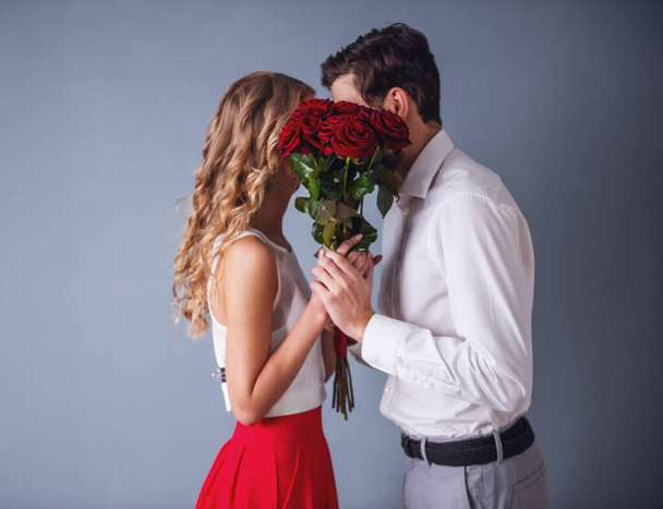 Hermosa pareja elegante se besa detrás de rosas, sobre fondo gris
 - Foto, imagen