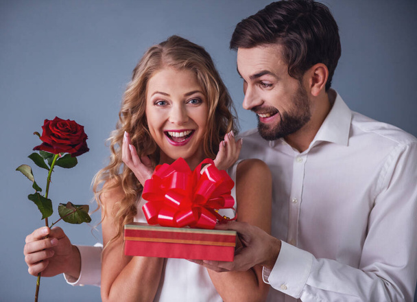 Bonito cara elegante está dando sua bela namorada caixa de presente e rosa e sorrindo
 - Foto, Imagem