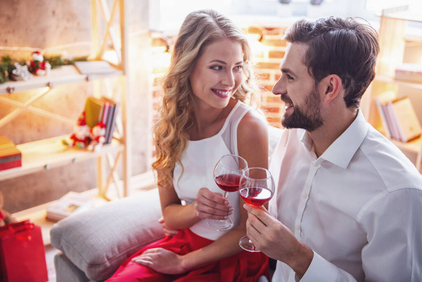 Belo jovem casal está segurando copos de vinho e sorrindo enquanto celebra em casa
 - Foto, Imagem