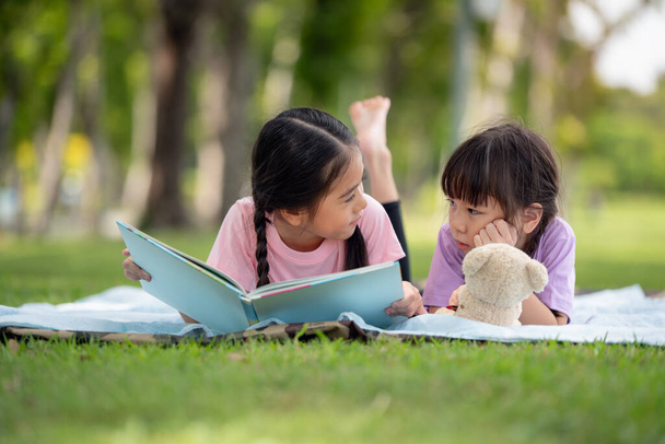 Feliz familia asiática niños leyendo un libro juntos en el parque - Foto, imagen