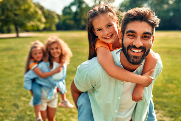 Onnellinen nuori perhe isä, äiti ja kaksi tytärtä leikkii puistossa niityllä lämpimänä aurinkoisena päivänä, pitää hauskaa yhdessä ja rentoutua vapaapäivänä.. - Valokuva, kuva