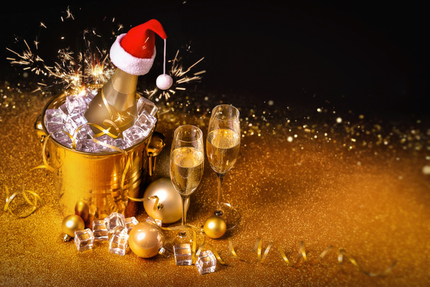 Een fles champagne in een gouden emmer met ijs en twee glazen op een zwart-gouden achtergrond. - Foto, afbeelding
