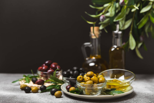 A set of green, red and black olives on a marble background. Various types of olives in bowls and fresh olive leaves. Vegan. Olive fruits. Place for text. Copy space. - Photo, Image
