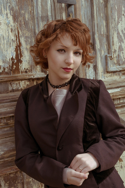 Retro portrait of red haired women in vintage coat agains obsolete wooden background - 写真・画像