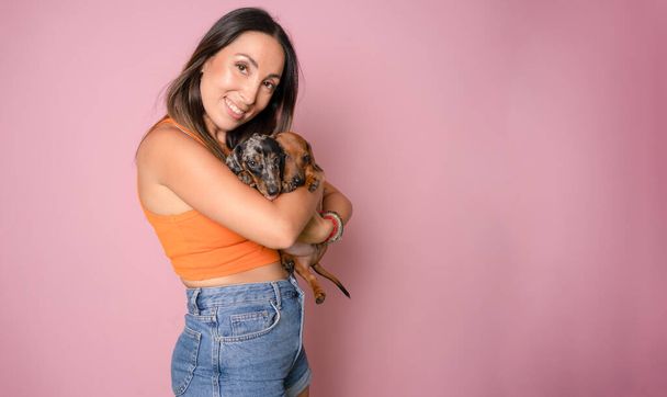 Young woman hugs her puppy Dachshund dogs . Love between dog and owner. Isolated on pink background. Studio portrait. - Photo, Image