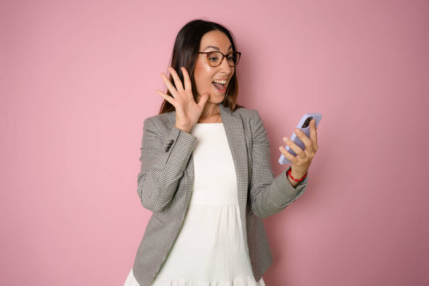 Portret van een lachende jonge zakenvrouw praten op mobiele telefoon geïsoleerd over roze achtergrond - Foto, afbeelding