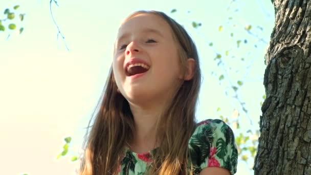 Portret van een lachend schattig meisje zittend op een boom in de zomer. - Video