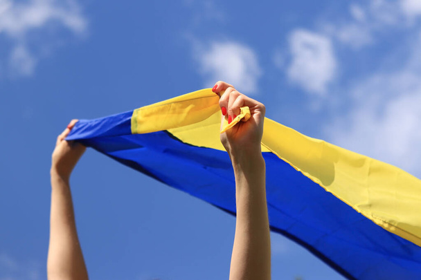 Une fille avec un drapeau jaune-bleu dans ses mains. Le drapeau flotte dans le vent. Patriotisme. Drapeau jaune et bleu de l'Ukraine dans les mains de la femme - Photo, image