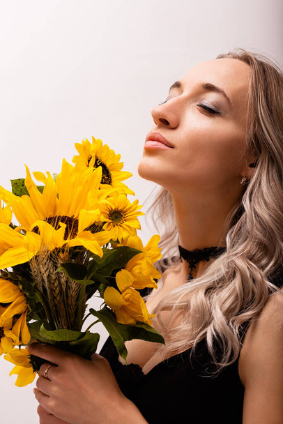 Nainen, jolla on silmät kiinni, nauttii itsestään, pitää kukkakimpun keltaisia kukkia. Auringonkukkakimppu. Laadukas kuva - Valokuva, kuva