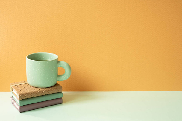 ミントグリーンデスクのノートとマグカップのスタック. オレンジ色の背景。 コピースペース - 写真・画像