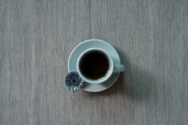Tasse Kaffee mit trockener Blume auf grauem Stoff Hintergrund. Ansicht von oben, Kopierraum - Foto, Bild