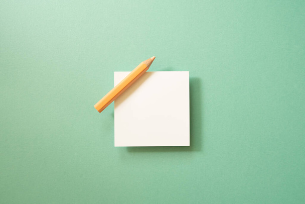 Білий папір-мемо, липкий блокнот з кольоровим олівцем на зеленому тлі. вид зверху, місце для копіювання - Фото, зображення