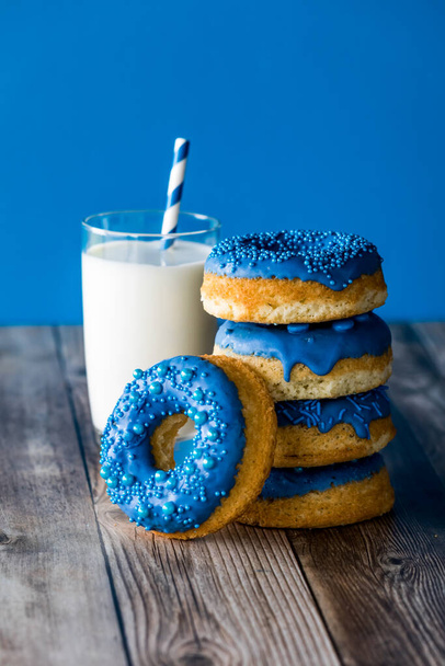 Μια στοίβα καραμέλες μπλε σοκολάτας βουτηγμένα ντόνατς με ένα ποτήρι γάλα, σε ένα μπλε φόντο. - Φωτογραφία, εικόνα