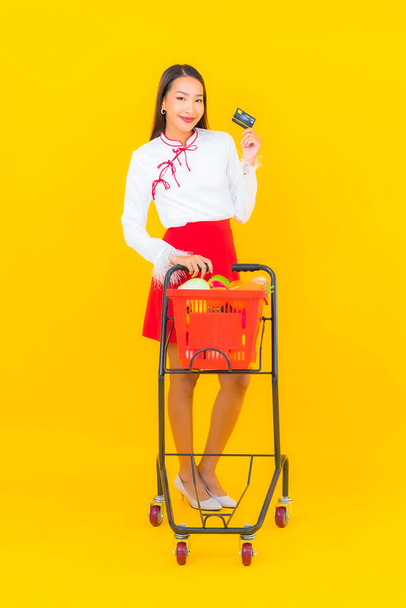 黄色の背景にスーパーマーケットから食料品バスケットと肖像美しい若いアジアの女性 - 写真・画像