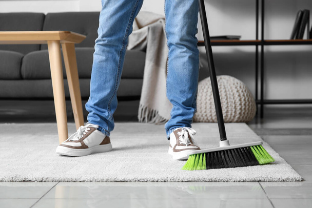 Young man sweeping carpet with broom at home - Photo, Image