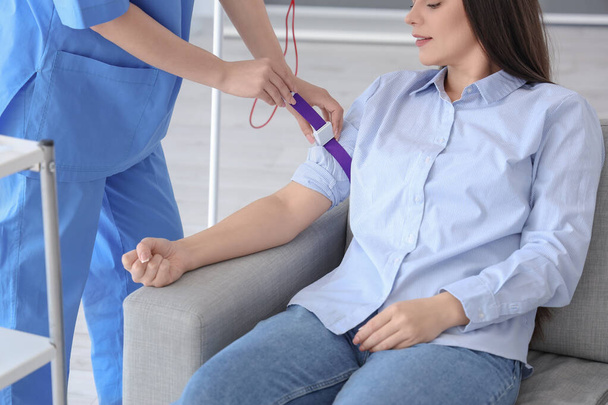 Θηλυκή νοσοκόμα προετοιμασία νεαρού δότη για μετάγγιση αίματος στην κλινική - Φωτογραφία, εικόνα