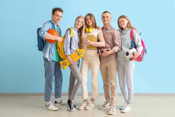 Группа студентов с рюкзаками и спортивным инвентарем возле синей стены - Фото, изображение