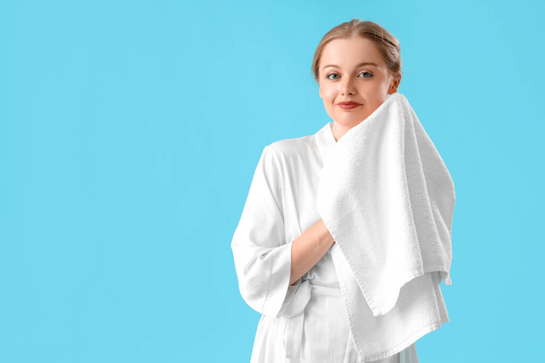 Ładna młoda kobieta z miękkim ręcznikiem na niebieskim tle - Zdjęcie, obraz