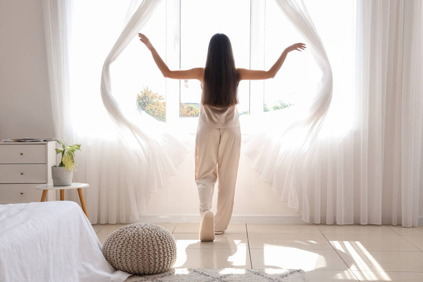 Утро красивой молодой женщины, открывающей шторы в спальне - Фото, изображение