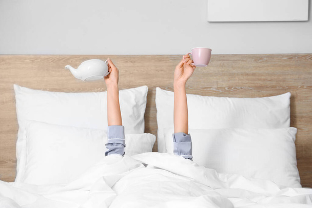 Πρωί της νεαρής γυναίκας με φλιτζάνι και τσαγιέρα στο κρεβάτι - Φωτογραφία, εικόνα