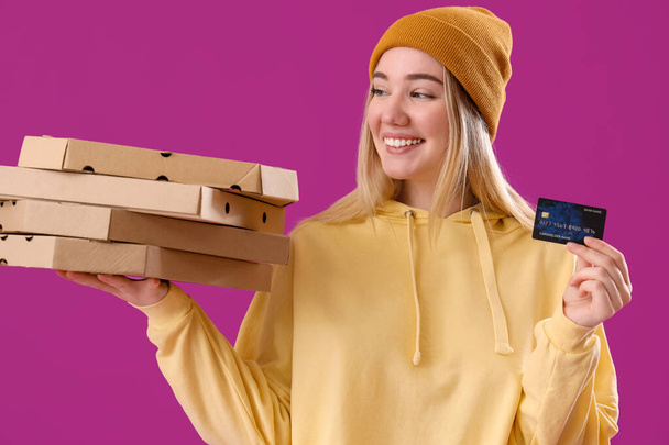 Junge Frau mit Kreditkarte und Pizzakartons auf lila Hintergrund - Foto, Bild