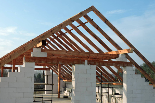 Una armadura de techo de madera en una casa en construcción, paredes hechas de bloques de hormigón aireado en autoclave, una abertura áspera de la ventana, un dintel de ladrillo reforzado, un andamio, cielo azul en el fondo - Foto, imagen