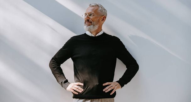 Portrait of confident mature man in smart casual wear holding hands on hip while standing against a wall - Foto, afbeelding