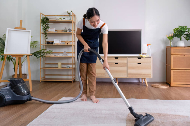 Giovane casalinga sta pulendo il pavimento del soggiorno con un aspirapolvere.. - Foto, immagini