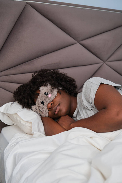 Beyaz çarşafların üzerinde tatlı bir uyku maskesiyle uyuyan Afrikalı genç bir kadın. Uyuyor.. - Fotoğraf, Görsel