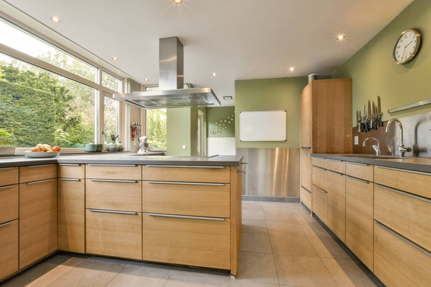 una cocina moderna con armarios de madera y electrodomésticos de acero inoxidable en los mostradores delante de la ventana es una vista exterior - Foto, Imagen