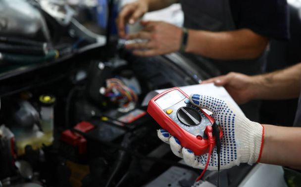 Крупный план мужских рук, проверяющих напряжение автомобильной батареи под капотом с точностью. Automechanic с использованием современной утилиты. Концепция автомобильного контроля
 - Фото, изображение