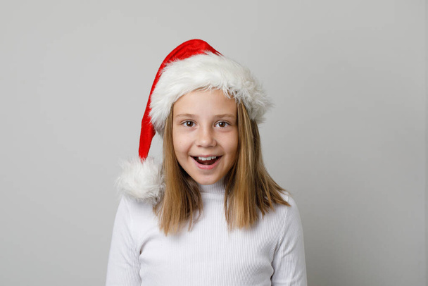 Χαρούμενη έκπληξη κοριτσάκι Άγιος Βασίλης διασκεδάζει σε λευκό φόντο - Φωτογραφία, εικόνα