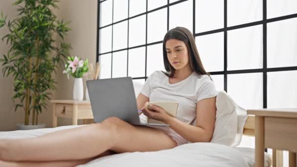 Laptop kullanan genç ve güzel bir İspanyol kadın yatak odasında not alıyor. - Video, Çekim