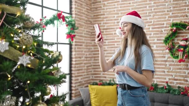 Young beautiful hispanic woman taking photo to christmas tree by smartphone at home - Footage, Video