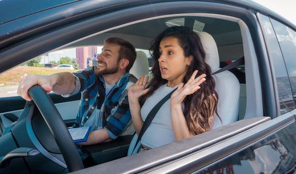 Άντρας εκπαιδευτής κρατώντας το χέρι του στο τιμόνι, ενώ η γυναίκα κάθεται στο αυτοκίνητο και την οδήγηση με την αλληλεπίδραση έκπληκτος. Δοκιμή οδήγησης, μαθήματα οδήγησης, εξεταστική έννοια - Φωτογραφία, εικόνα