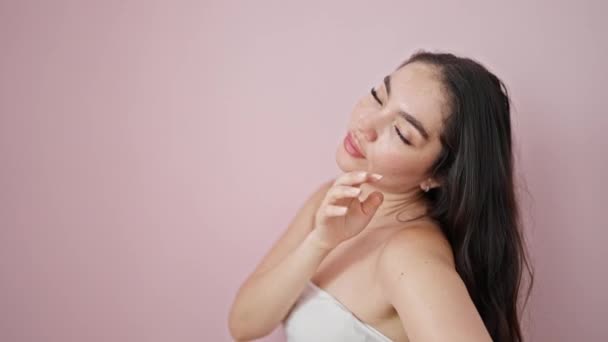 Νεαρή όμορφη ισπανόφωνη γυναίκα αγγίζει το πρόσωπο πάνω από απομονωμένο ροζ φόντο - Πλάνα, βίντεο