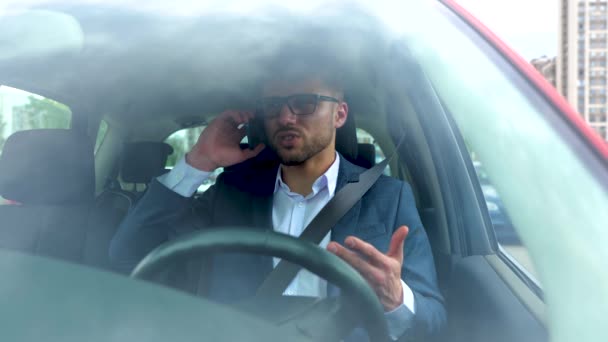 Rozrušený mladý stylový muž v obleku mluví po telefonu, zatímco sedí na sedadle řidiče a zapíná bezpečnostní pás. Koncept dopravy, obchodu, technologií a lidí. Zpomalený pohyb - Záběry, video