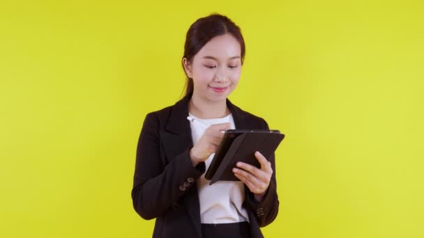 Portret jonge Aziatische zakenvrouw in pak staan met behulp van tablet computer schrijven record op internet op gele achtergrond, zakenvrouw op zoek naar digitale tablet met succes, communicatie concept. - Video