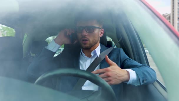 Hombre de negocios ocupado sentado en el asiento del conductor en el coche mientras habla en el teléfono inteligente. Concepto de transporte, negocios, tecnología y personas. Movimiento lento - Metraje, vídeo